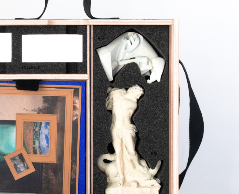 Valise vue de l'intérieur. Elle contient une version miniature d'une statut en marbre représentant Hercule qui combat un lion, un petit robot, des photos de tableaux.