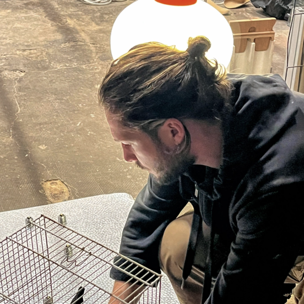 Vincent Gallais est de profil et travaille sur une sculpture : il est concentré et il installe une cage en fer sur un support en acier.