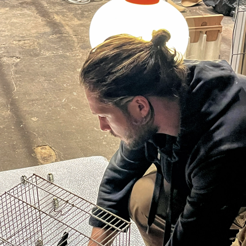 Vincent Gallais est de profil et travaille sur une sculpture : il est concentré et il installe une cage en fer sur un support en acier.